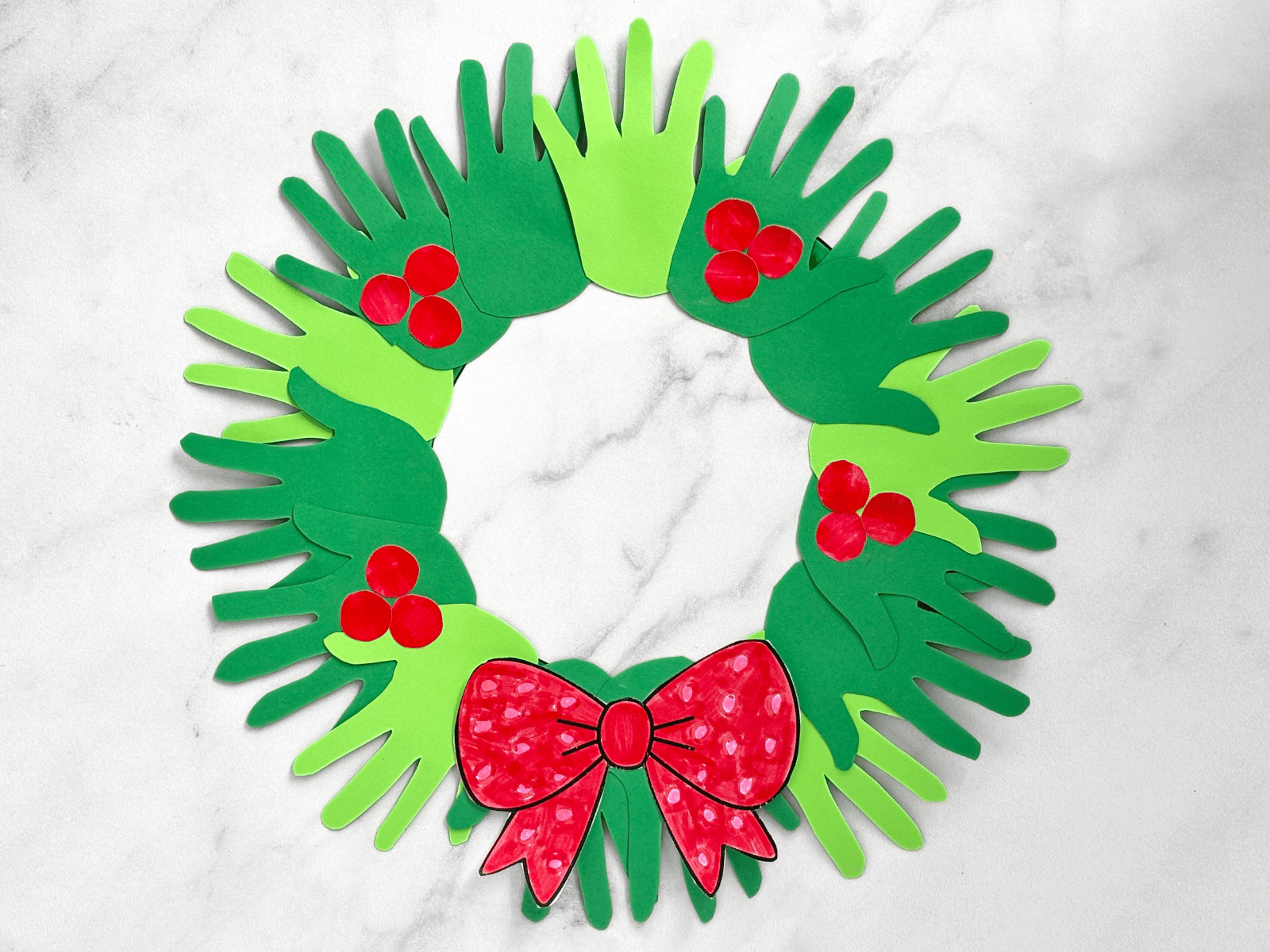 Handprint wreath craft for kids made from green handprints arranged in a circle with red berries